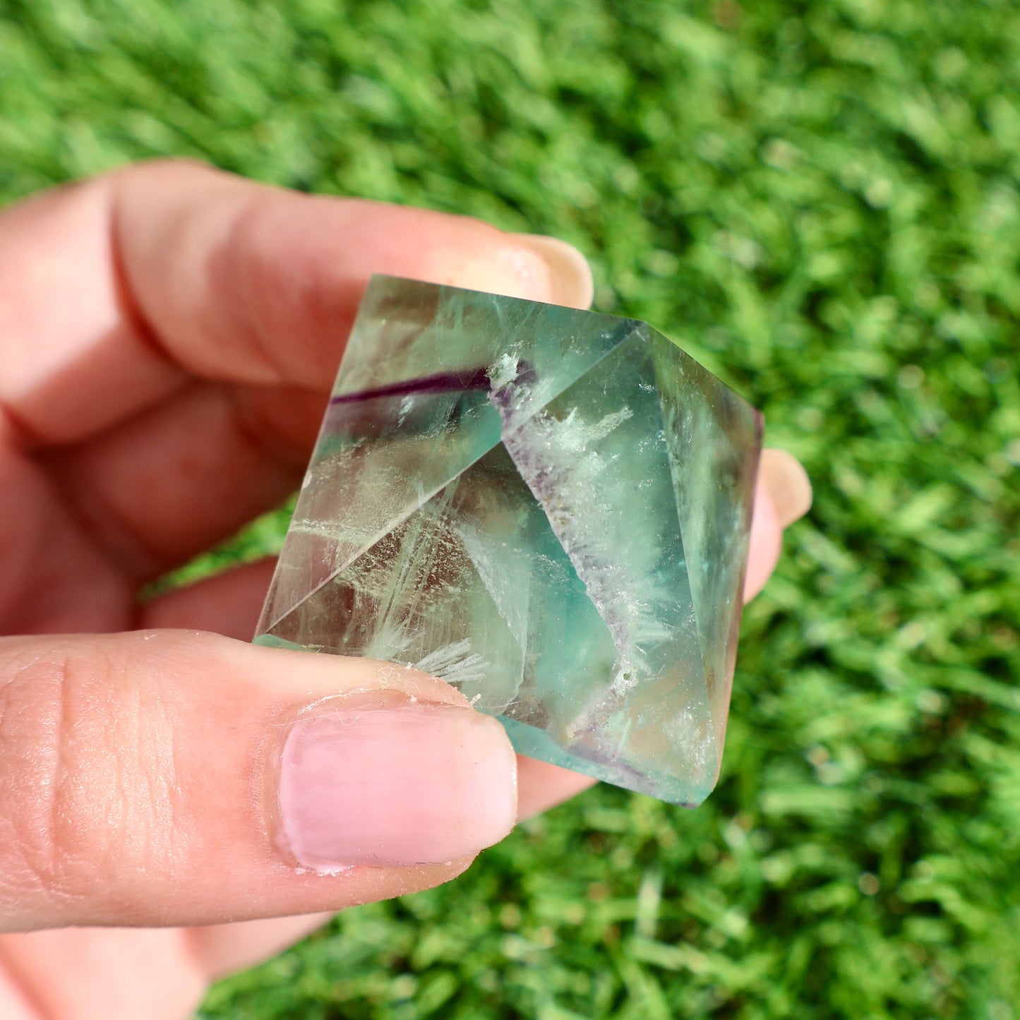 green and purple fluorite pyramids on grass, 1-inch crystal cut