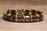 A beaded bracelet with alternating dark gray hematite rectangular beads and round gold hematite beads, displayed on a wooden surface.